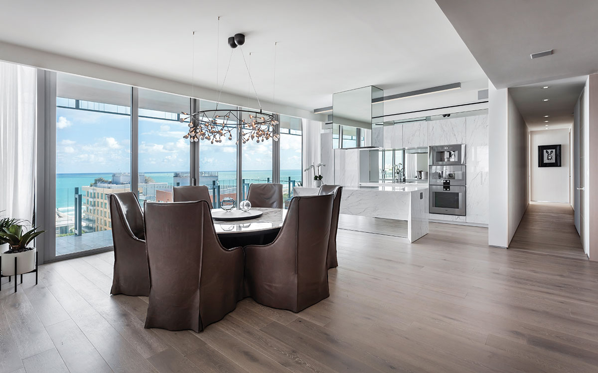 In the dining area, mushroom-colored leather-clad chairs from Verellen create a dramatic contrast near a bright kitchen with white-veined marble cabinetry. A Bertjan Pot for Moooi chandelier from Planet Lighting glitters above Maxalto’s marble table enhancing the ocean view through floor-to-ceiling windows.