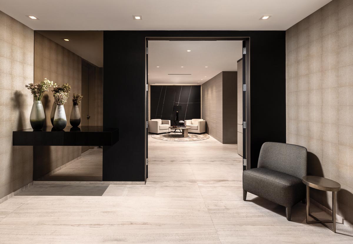 The entrance to the Armani Casa Residences condominium embodies a refined, masculine aesthetic requested by the homeowner. Taupe leather wallpaper melds with a bronze mirror against floating black drawers. A dramatic Azalai Negro porcelain slab highlights the back wall of the conversation area, where Armani/Casa furnishings center around a plush Stark rug.